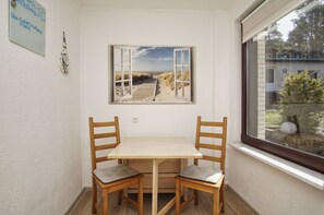 Una habitación de esquina con una mesa y sillas de madera, una ventana con vista a la playa y un cuadro en la pared.