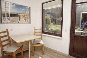 Una habitación con una mesa y sillas de madera, una ventana con vista a un jardín y una puerta que da a un tobogán.