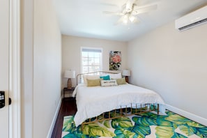 A bedroom with a bed, a ceiling fan, an air conditioner, a window, and a door.
