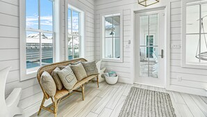A room with a wicker sofa, a glass door leading outside, and a view of a building through the window. - Stunning Palmilla Beach home with gulf views, private pool, and golf (Port Aransas)