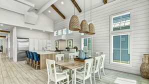 A spacious kitchen with white cabinetry, a wooden dining table, and hanging wicker pendant lights. - Stunning Palmilla Beach home with gulf views, private pool, and golf (Port Aransas)
