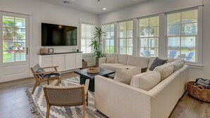 A spacious living room with a large flat-screen TV, a beige sofa, a coffee table, and a ceiling fan.