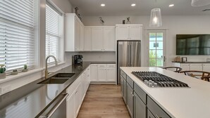 A modern kitchen with white cabinetry, stainless steel appliances, and a large island with a built-in stove.