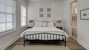 A bedroom with a bed, white walls, and a wooden floor.
