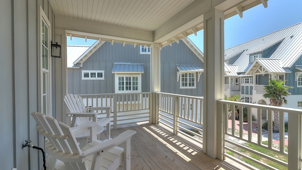 A covered porch with white Adirondack chairs, a metal railing, and a view of neighboring houses.