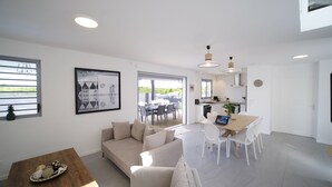 A modern living room with a sofa, dining table, and chairs. There is a kitchen area with a stove and sink. - Architect designed villa for 8 with swimming pool (Saint François)