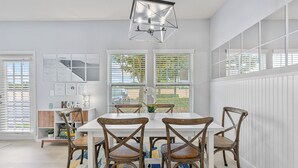 A dining area with a white table, six wooden chairs, a colorful rug, and a modern pendant light.