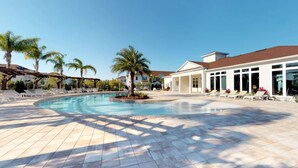 A swimming pool with sun loungers and palm trees, surrounded by a building with large windows.