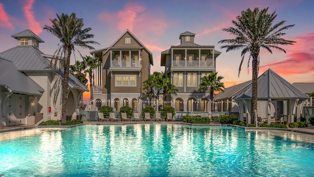 A large swimming pool surrounded by two-story buildings with balconies, palm trees, and a sunset sky. - Luxe Palmilla townhome with resort pool & golf - walk to beach (Port Aransas)