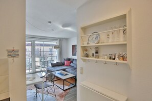 Una sala de estar moderna con un sofá, una mesa de centro y sillas. Una ventana grande ofrece vistas al exterior.