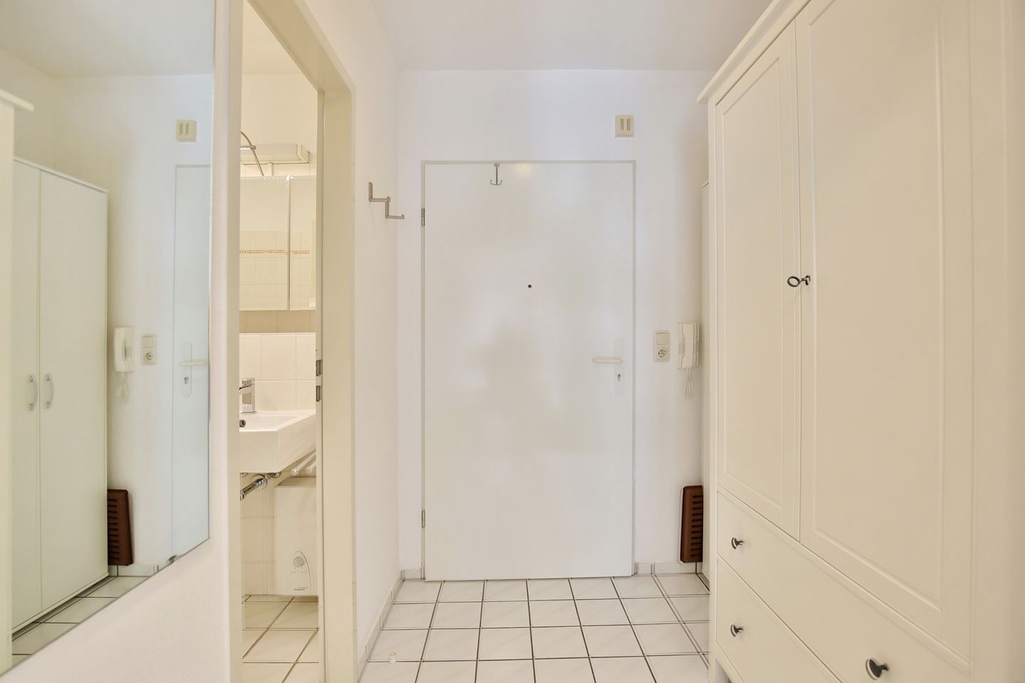 Un corridoio con una porta bianca, uno specchio e un pavimento piastrellato.