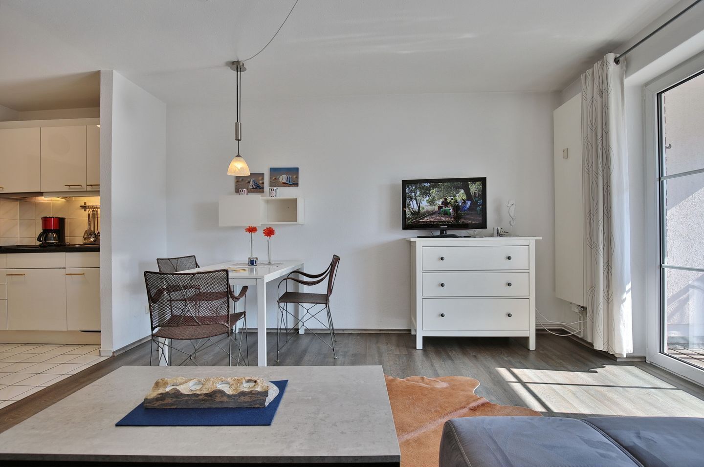 A modern living room with a dining area, a TV, and a kitchen in the background.