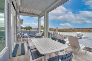 Eine überdachte Terrasse mit Tisch und Stühlen mit Blick auf ein Gewässer und eine entfernte Landschaft.
