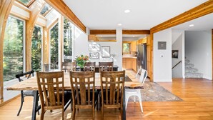 A spacious dining area with wooden chairs and a table, large windows, and a view of the outdoors.