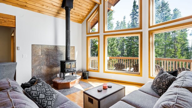 A cozy living room with a fireplace, large windows, and a balcony with a wooden railing.