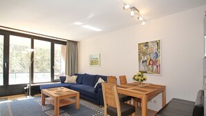 Un salon moderne avec un canapé, une table à manger et des chaises. On y trouve une grande fenêtre avec des rideaux, un tableau au mur et un radiateur.