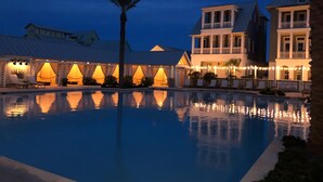 A swimming pool with a reflection, surrounded by buildings with balconies and string lights. - Palmilla | Fairway-View Balcony | Heated Pool, Golf & Private Beach Access (Port Aransas)