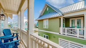 A green building with a balcony and a covered porch area with blue chairs. - Palmilla | Fairway-View Balcony | Heated Pool, Golf & Private Beach Access (Port Aransas)