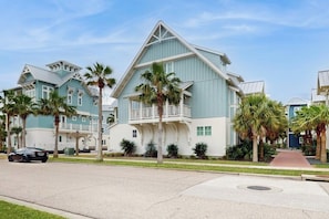 A coastal-style building with a balcony, palm trees, and a clear sky.