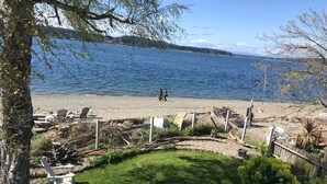 A beach with a grassy area, white lounge chairs, and a view of the water. - Prime Sandy Beachfront Home with Mountain Views - 5 minutes to Gig Harbor/Tacoma (Gig Harbor)