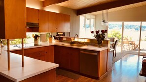 A modern kitchen with wooden cabinets, a central island, and a view of the outdoors. - Prime Sandy Beachfront Home with Mountain Views - 5 minutes to Gig Harbor/Tacoma (Gig Harbor)