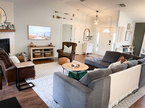 Una sala de estar moderna con chimenea, sillón de cuero, sofá gris y mesa de centro de madera.