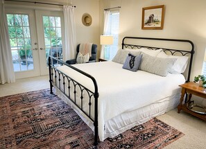 Een slaapkamer met een bed, een stoel, een lamp, een foto aan de muur en een raam met gordijnen.