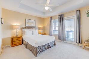 Une chambre à coucher avec un grand lit, deux tables de chevet avec des lampes, un ventilateur de plafond et une fenêtre avec des rideaux.