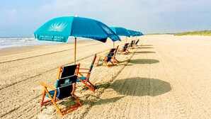 Ein Strand mit Reihen von Liegestühlen und Sonnenschirmen, wobei jeder mit „Palmilla Beach Resort & Golf Community“ beschriftet ist.