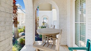 Ein überdachter Patio-Bereich mit rundem Tisch und Stühlen, weißen Backsteinwänden und Blick auf die umliegende Nachbarschaft.