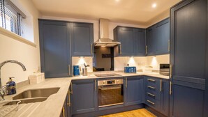 A modern kitchen with dark blue cabinets, stainless steel appliances, and a wooden floor. - Skyway First Floor Apartment is a 2 bedroom apartment with parking in Three Bridges (West Sussex)