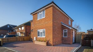 A two-story brick house with a front garden, a car parked in the driveway, and a wooden fence. - Skyway First Floor Apartment is a 2 bedroom apartment with parking in Three Bridges (West Sussex)