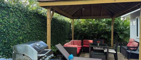 Un patio extérieur couvert, équipé d’un barbecue, d’un espace salon et d’une structure en forme de pergola.
