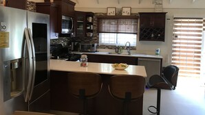 A kitchen with a refrigerator, stove, microwave, and a ceiling fan. There are two bar stools and a window with blinds. - Sweet Oasis - gated with 24/hr security/ swimming pool/ free access to beach  (Saint Ann's Bay)
