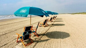 Ein Strand mit Reihen von Liegestühlen und Sonnenschirmen, jeweils mit "Palmilla Beach Resort & Golf Community" beschriftet.