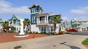 A residential area with a prominent blue house featuring a tower, a red truck, and a well-maintained driveway. - Palmilla Beach designer retreat with golf, pool & chef's kitchen - walk to beach (Port Aransas)
