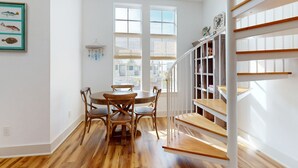 A dining area with a wooden table and chairs, a staircase with wooden steps, and a view of the outside through large windows. - Palmilla Beach designer retreat with golf, pool & chef's kitchen - walk to beach (Port Aransas)