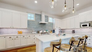A modern kitchen with white cabinets, a large island with bar stools, a microwave, and a gas stove. - Palmilla Beach designer retreat with golf, pool & chef's kitchen - walk to beach (Port Aransas)