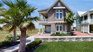Una casa a due piani con un portico coperto, un piccolo balcone e un giardino anteriore curato con palme e un vialetto.