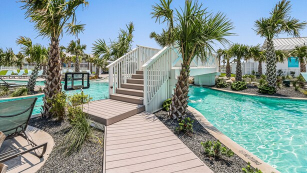 A pool area with a wooden deck, palm trees, and a staircase leading to a building. - Golf-View Palmilla Beach retreat with pool, private garage, & alfresco dining (Port Aransas)