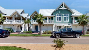 A row of two-story houses with white balconies and green roofs, parked on a street. - Golf-View Palmilla Beach retreat with pool, private garage, & alfresco dining (Port Aransas)