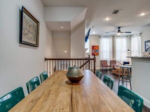 A dining area with a wooden table, green chairs, a vase centerpiece, and a staircase leading to another level.