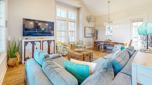 A spacious living room with a large TV, comfortable seating, and a dining area with a table and chairs. - Palmilla Beach gem - 2 luxe suites, 2 balconies, pools, golf-course views & w/d (Port Aransas)