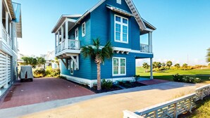 A two-story house with a balcony, a covered driveway, and a well-maintained lawn. - Palmilla Beach gem - 2 luxe suites, 2 balconies, pools, golf-course views & w/d (Port Aransas)