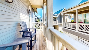 A wooden deck with Adirondack chairs, a railing, and a view of neighboring houses. - Palmilla Beach gem - 2 luxe suites, 2 balconies, pools, golf-course views & w/d (Port Aransas)