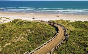 Meander along a wooden boardwalk to a serene beach surrounded by lush greenery.