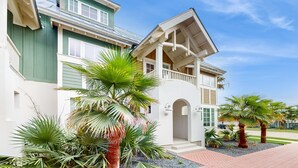 A two-story house with a balcony, surrounded by palm trees and a paved driveway.