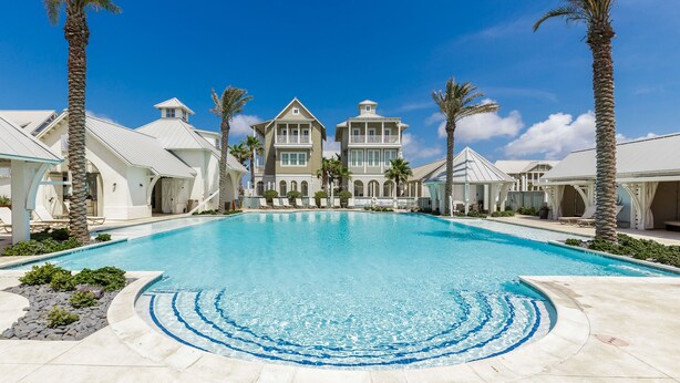 A large swimming pool surrounded by palm trees and a grand building with multiple balconies.