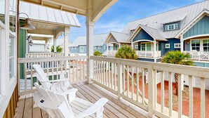 A covered porch with white Adirondack chairs and a view of blue and white houses with a metal roof.