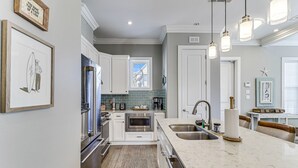 Una cocina moderna con armarios blancos, electrodomésticos de acero inoxidable, encimera de mármol e iluminación colgante.